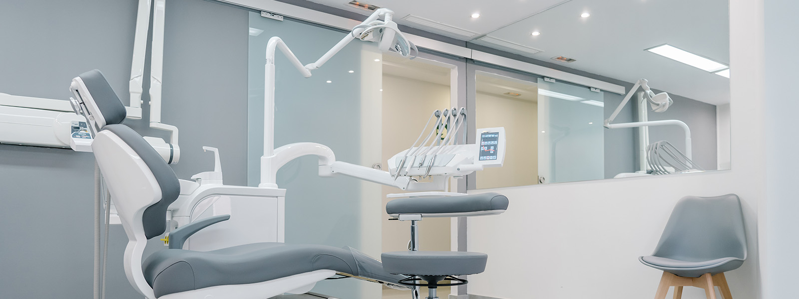 The image shows an interior view of a dental office with various dental equipment, including chairs, tables, and a large window with a view of the outside.