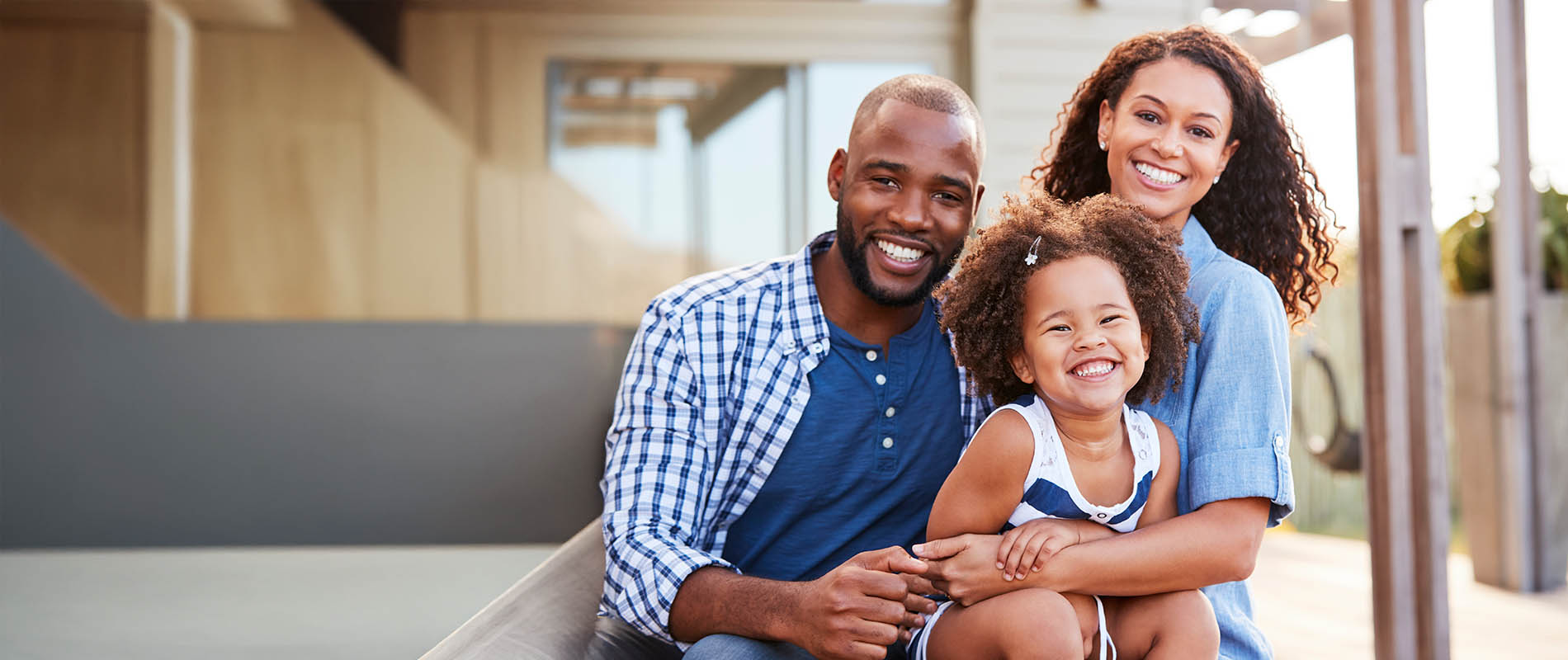 A family of three poses together outdoors with a relaxed and happy expression.