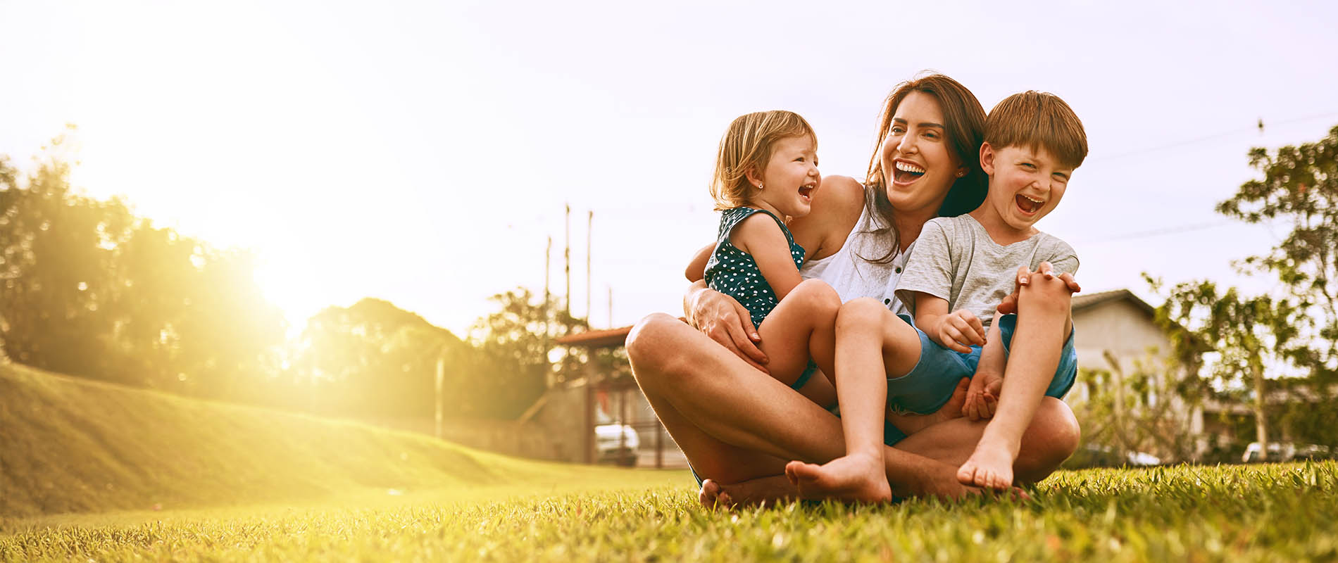 A family sitting together on grass, smiling at the camera with a sunny backdrop.