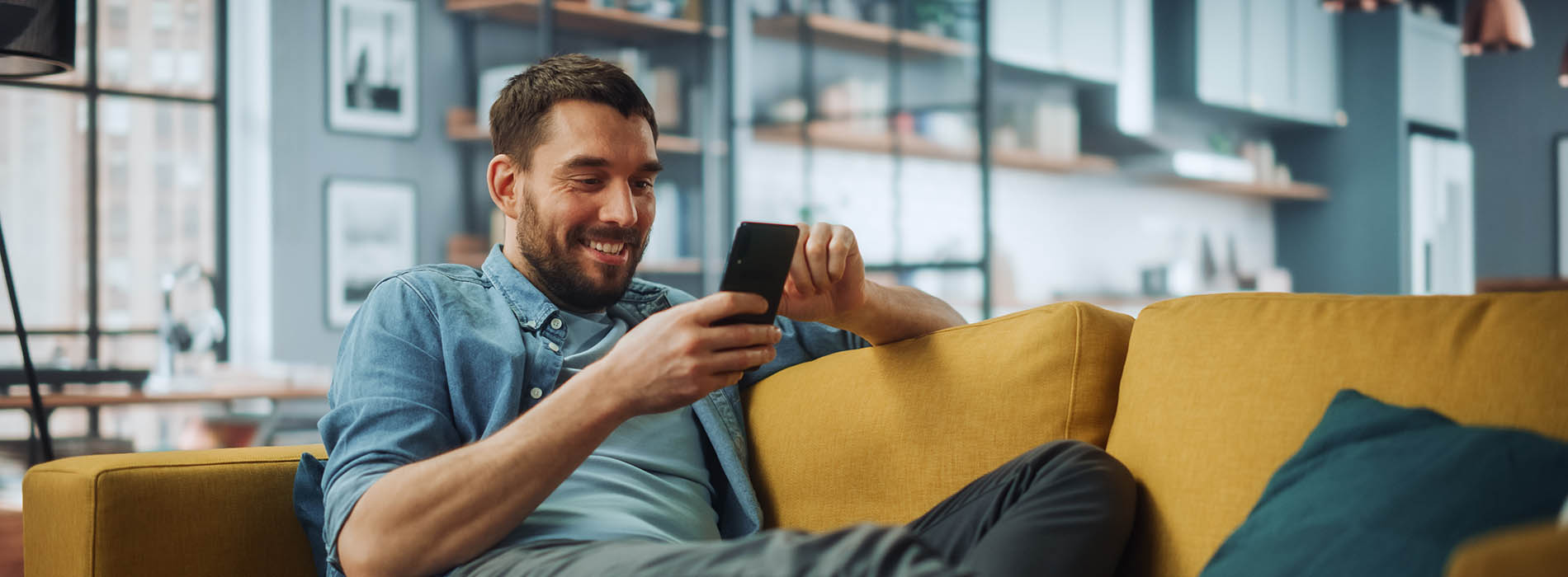 A man sitting on a couch with a smartphone in his hand, looking at the screen.
