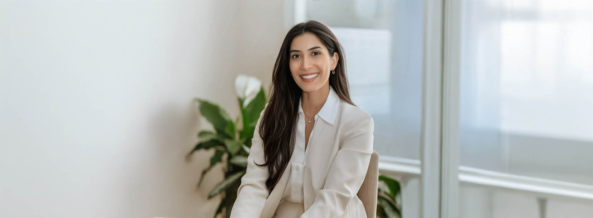 The image shows a woman sitting in an office environment, smiling at the camera.