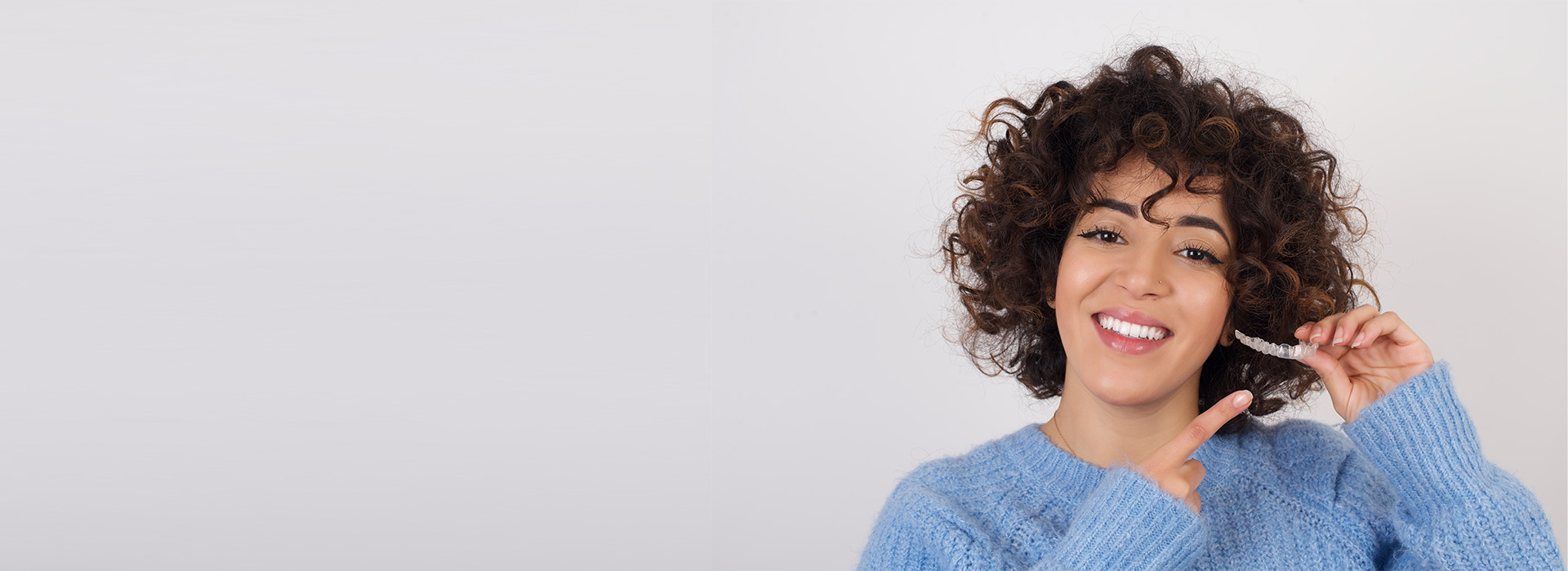 The image shows a person with curly hair smiling at the camera while holding a toothbrush. They are wearing a blue sweater, and there is text overlaying the image that reads  LIFE IS GOOD  in white letters.