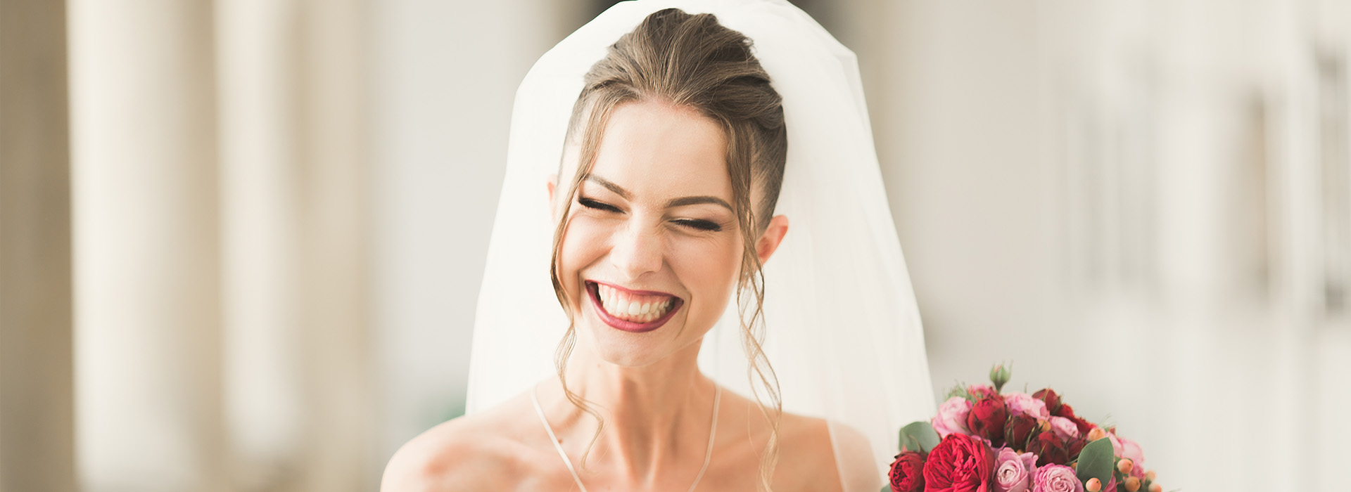 A bride wearing a white wedding dress and veil, smiling at the camera, with a bouquet of flowers nearby.
