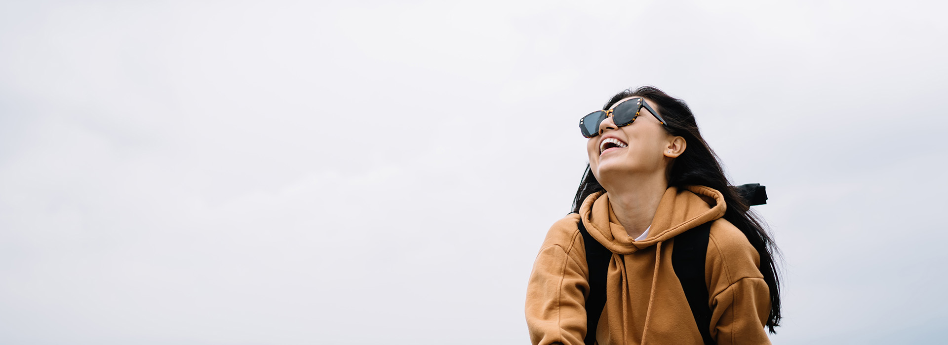 The image shows a person from behind, wearing sunglasses and a backpack, standing on a snowy surface with a cloudy sky above.