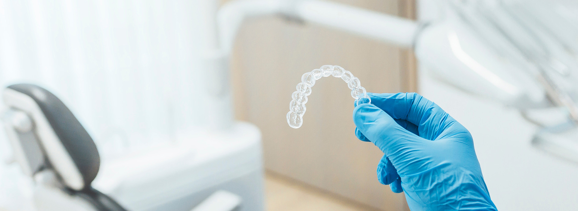 The image shows a hand holding a small white object, possibly a piece of medical equipment or a scientific sample, with gloves on, set against a blurred background that appears to be an indoor setting, likely a laboratory or a clean room.