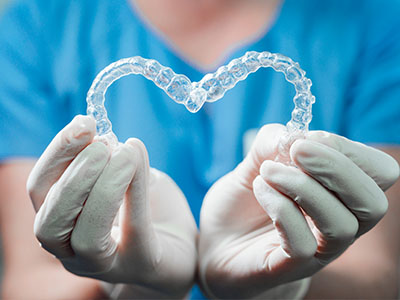 A hand holding a clear plastic heart-shaped object with an intricate pattern inside, against a blurred background.