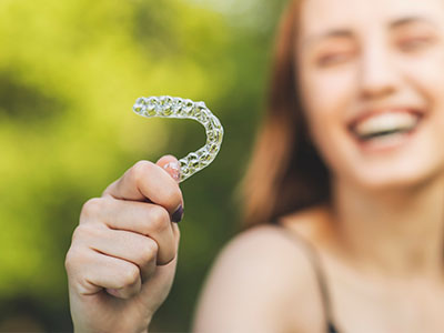 A person smiling while holding up a toothbrush with a smiley face design.