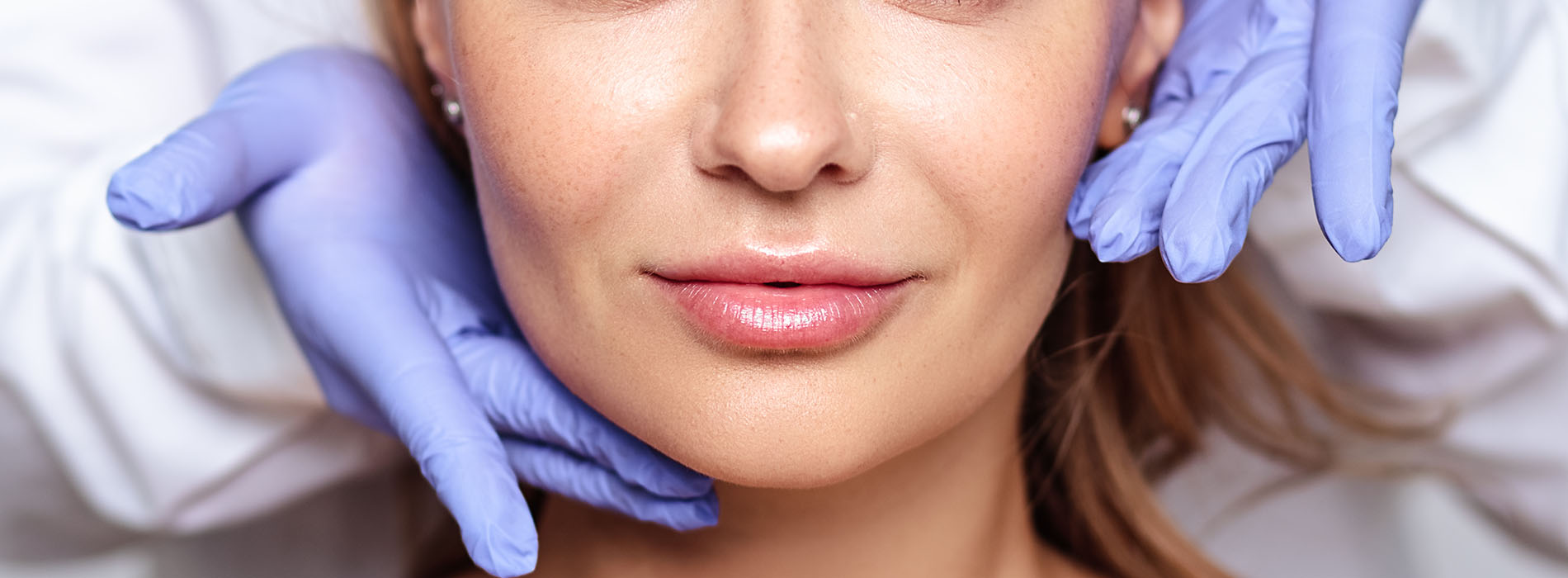 Woman receiving facial treatment with blue gloves visible on her hands.