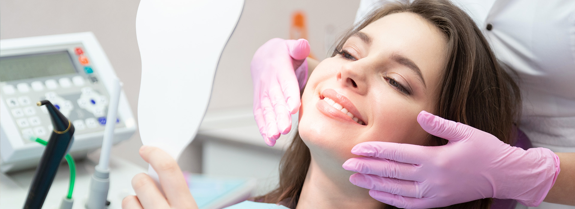 A woman sitting in a dental chair with a hygienist performing a cleaning procedure on her teeth, wearing protective gloves and using a dental mirror.