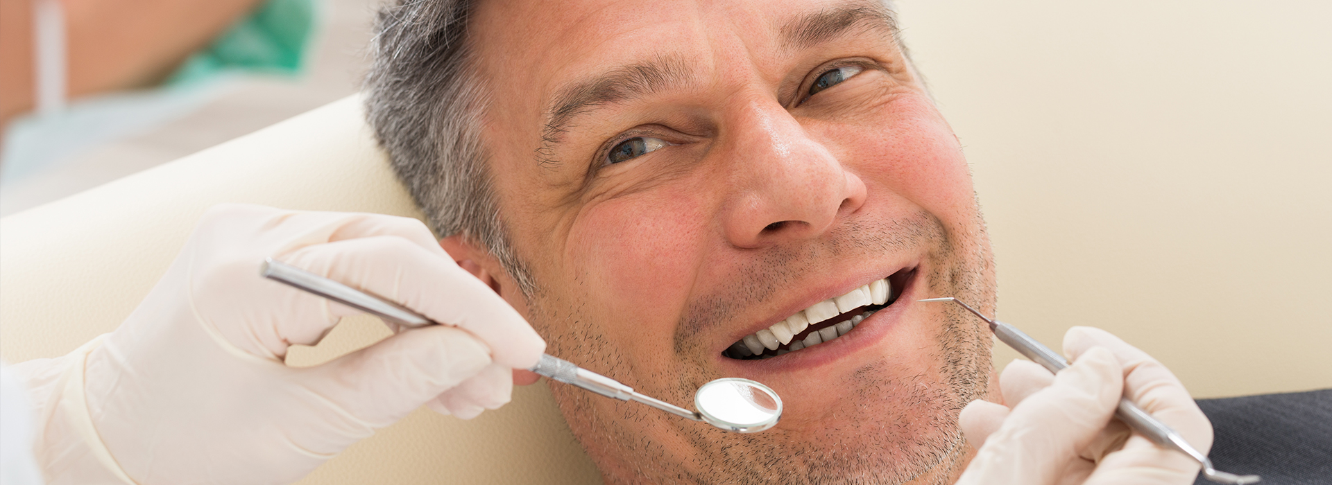 The image shows a man sitting in a dental chair receiving dental treatment, with a dentist working on his teeth using dental tools.