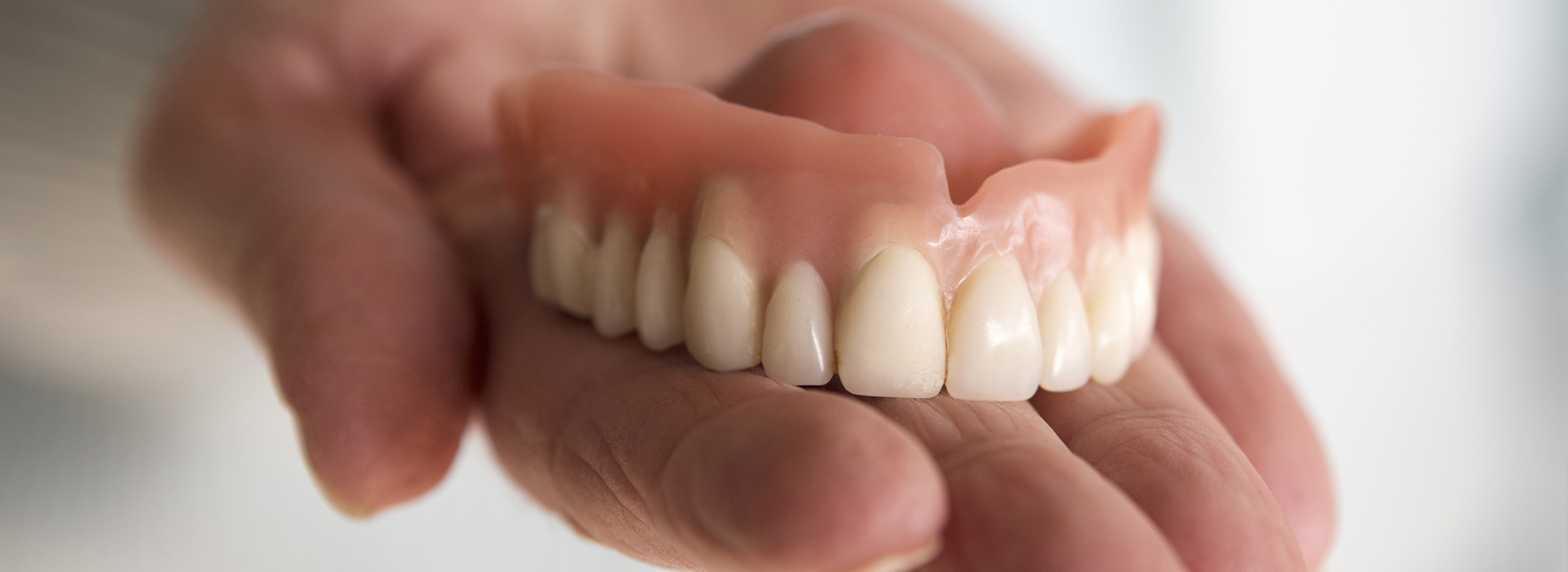 The image shows a hand holding an open mouth with a set of dentures inside, emphasizing the dental appliance.