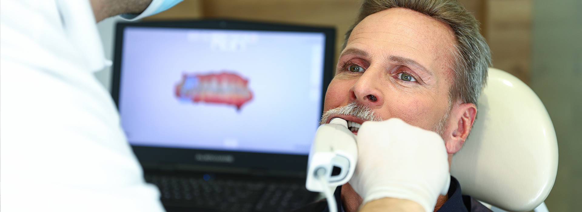 The image shows a man receiving medical attention at a dental clinic, with a dentist examining his teeth while he is seated in a chair and wearing a surgical mask.
