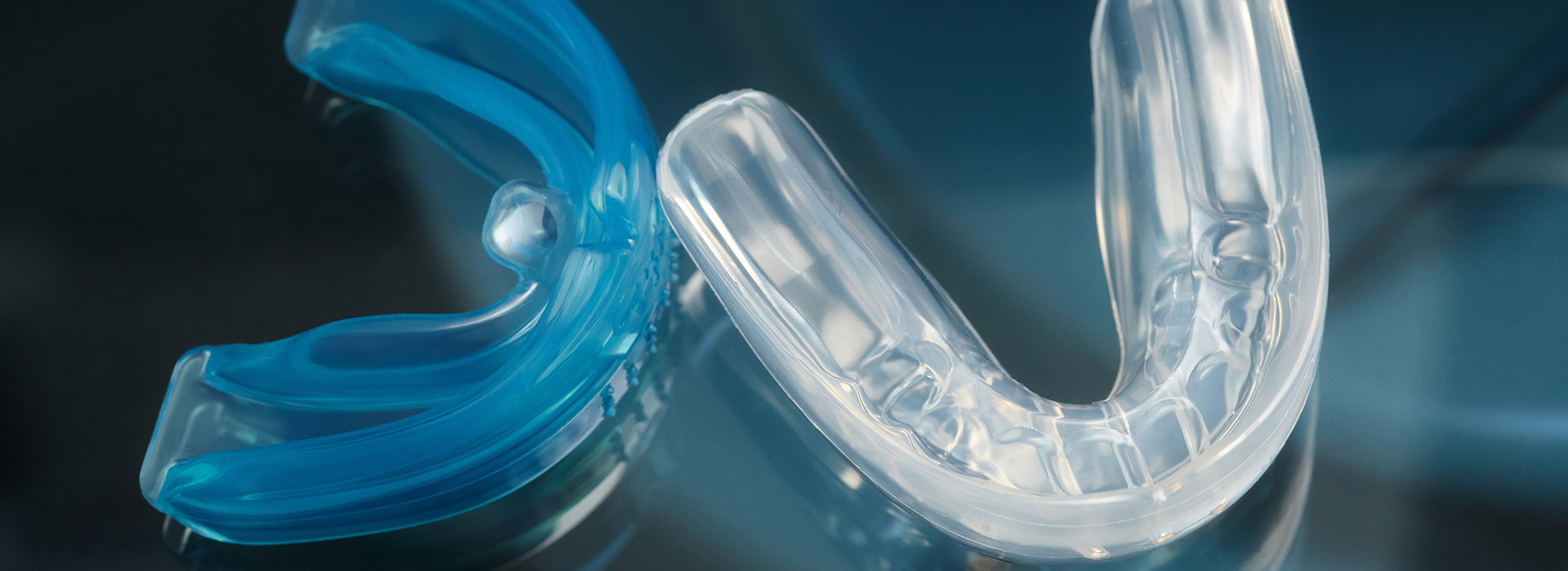 This is a close-up photograph showcasing two transparent plastic braces with blue accents against a blurred background, which appears to be an abstract design with cool tones.