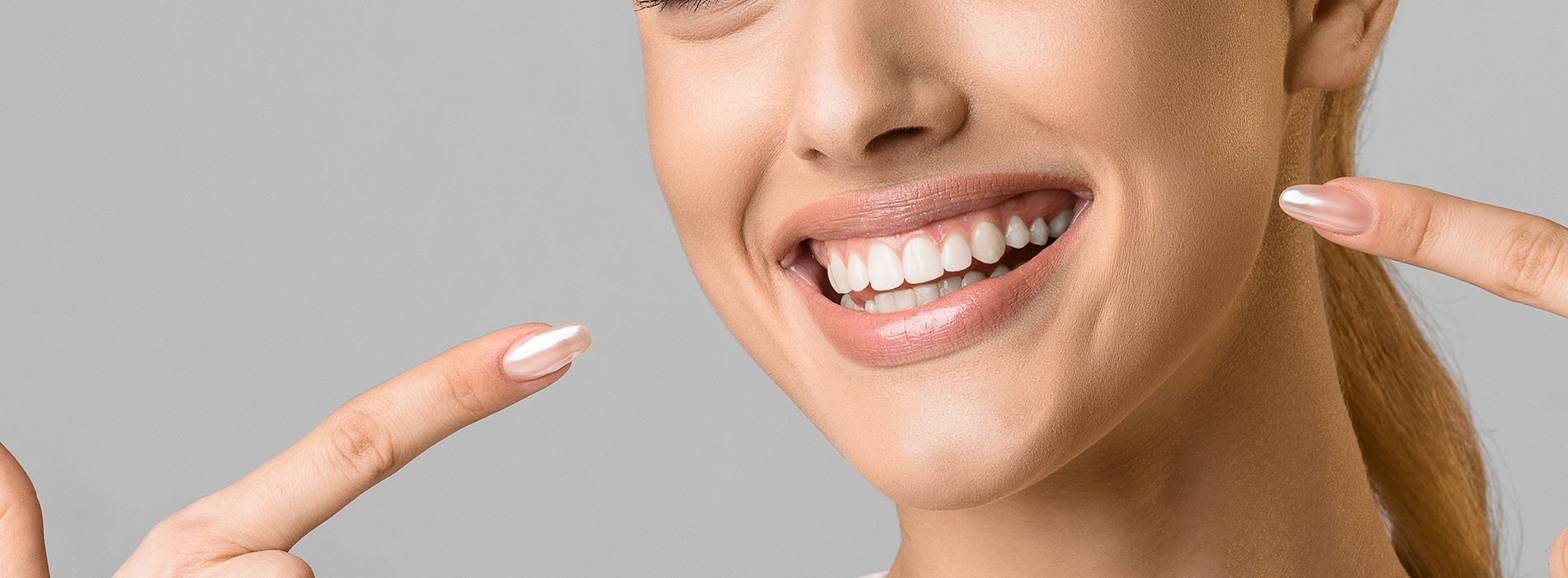The image shows a smiling woman with light skin holding up two fingers next to her face.