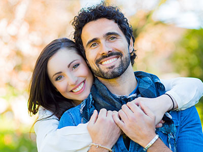 A smiling man and woman hugging each other outdoors.