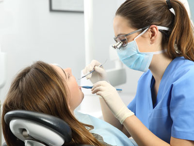 A dental hygienist performing a cleaning procedure on a patient s teeth while wearing protective eyewear and gloves.