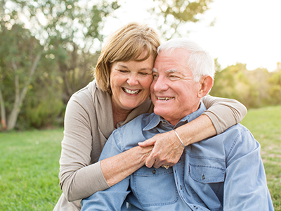 A man and woman are affectionately hugging each other outdoors during daylight hours.
