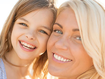 A photograph of two individuals, an adult and a child, smiling at the camera with a blurred background.