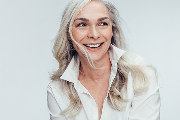 The image features a woman with short hair smiling at the camera, wearing a white shirt and leaning slightly towards the viewer.