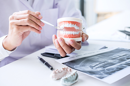 The image depicts two photos side by side  on the left, a dental professional wearing gloves holds a tooth model, while on the right, another person examines the same tooth model with a magnifying glass, both set against a backdrop of medical equipment and materials.