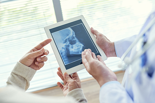 The image shows two people examining an X-ray on a tablet held by a medical professional, with a focus on the X-ray being displayed.