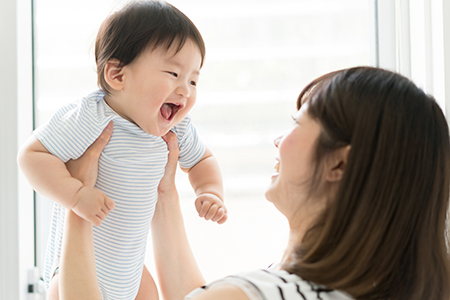 The image shows a woman holding a baby with a joyful expression while looking at the camera.