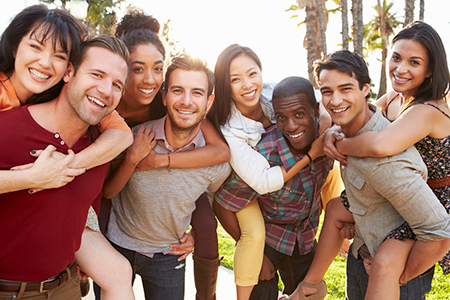 The image depicts a group of young adults posing together outdoors with smiles on their faces, embracing each other in a celebratory manner.
