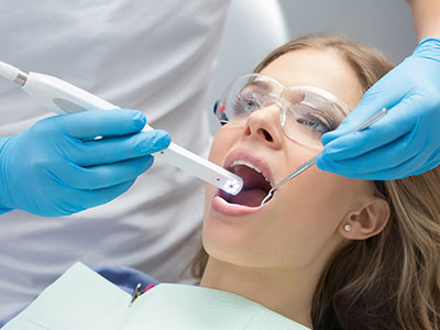 Woman receiving dental treatment with dental dam, dental mirror, and dental drill; dental professional assisting with procedure.