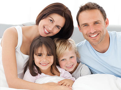 A family of four posing for a photo on a bed with a happy expression.