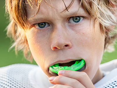 A photograph collage featuring two images: on top, a young boy with blond hair blowing a bubble; below, a close-up of his face with a green object in his mouth, likely a toothbrush.