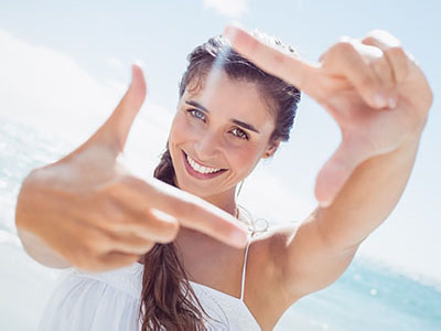A woman with long hair smiling at the camera while making a peace sign with her hand.