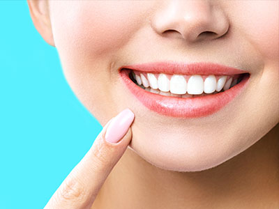 The image depicts a close-up of a person's smiling face with well-groomed teeth, against a plain blue background.